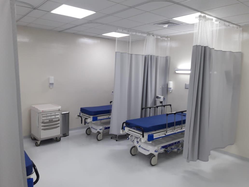 Sala de observación con camillas, cortinas divisorias y carro de insumos.